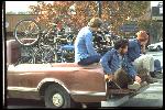 Fairfax Parkade, downtown Fairfax, bound for Repack. On Vince Carlton’s brown pickup truck, left to right,  Joe Breeze, Chris McManus, Mark Green, Ben Berto. Breezer  number 1 , primer red, on top of pile of bikes. 